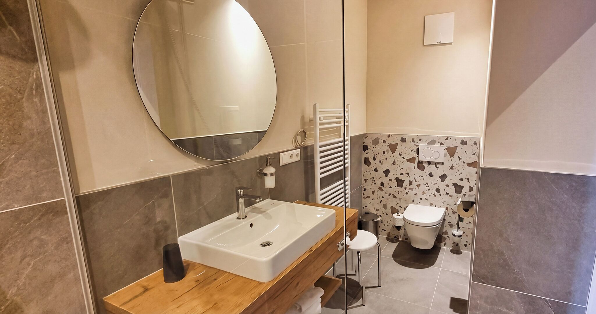 A modern bathroom with a wooden vanity, a large mirror, a toilet, and a shower area.