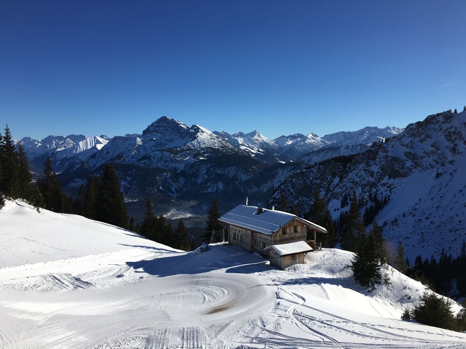 A snow-covered mountain landscape with a wooden cabin and a ski trail.
