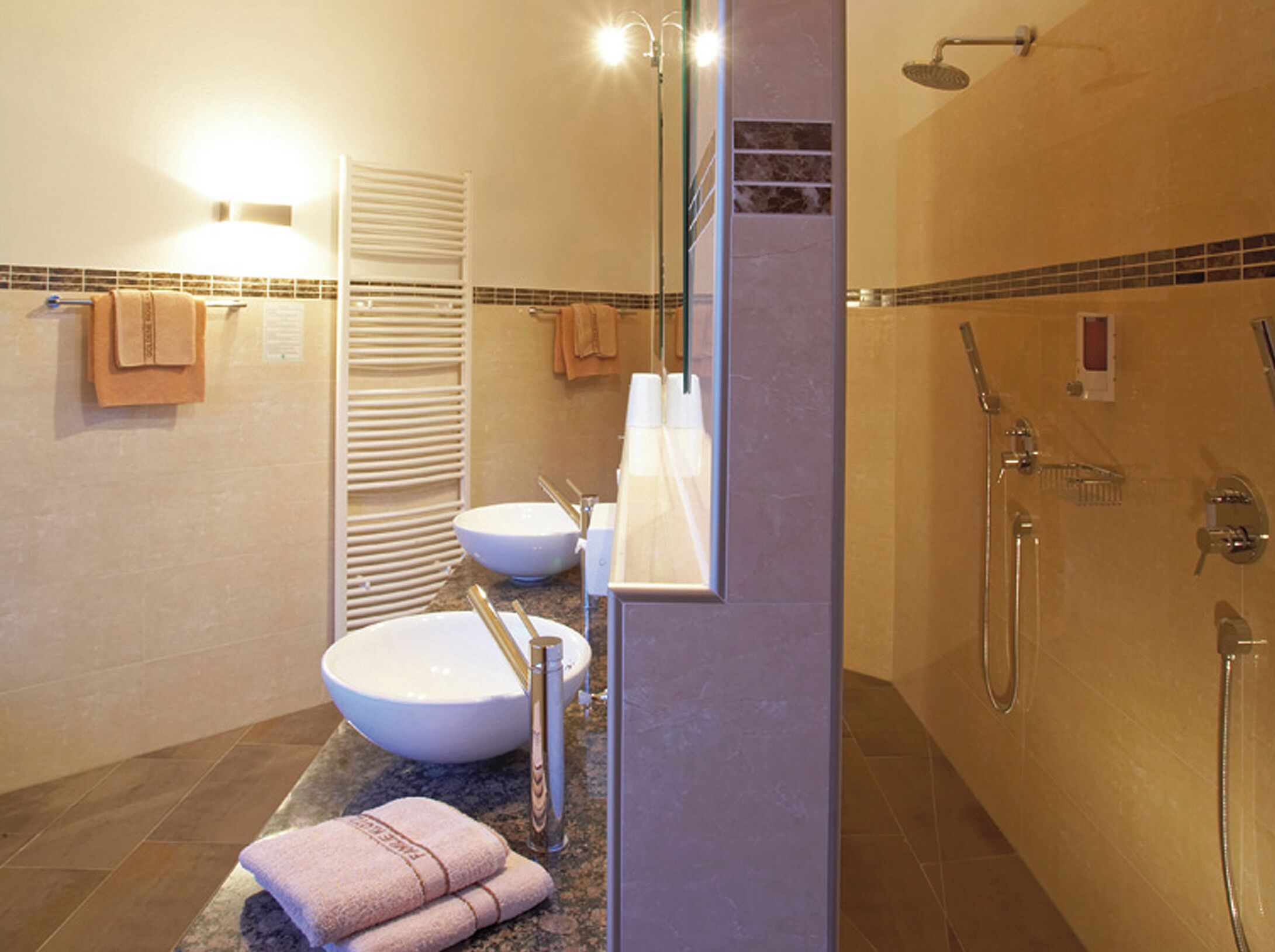 A bathroom with a large sink, a mirror, a shower, and towels on the floor.
