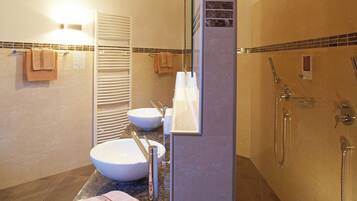 A bathroom with a large sink, a mirror, a shower, and towels on the floor.