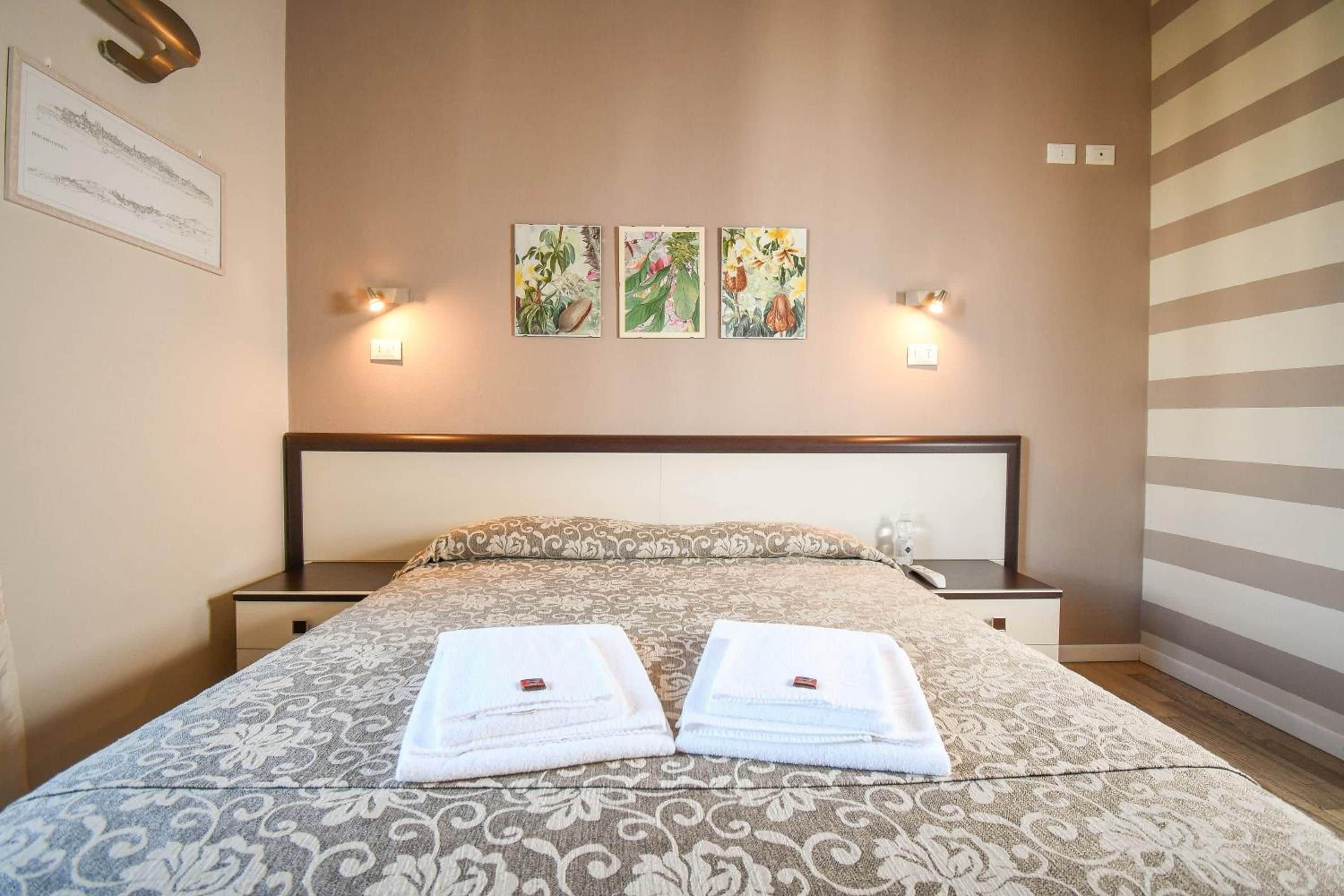 Una habitación de hotel con una cama, dos mesitas de noche y tres lámparas de pared.