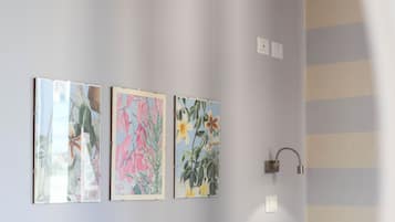 Une salle de bain avec trois œuvres d’art florales encadrées accrochées au mur, un porte-serviettes et une douche dotée d’un pommeau de douche incurvé.