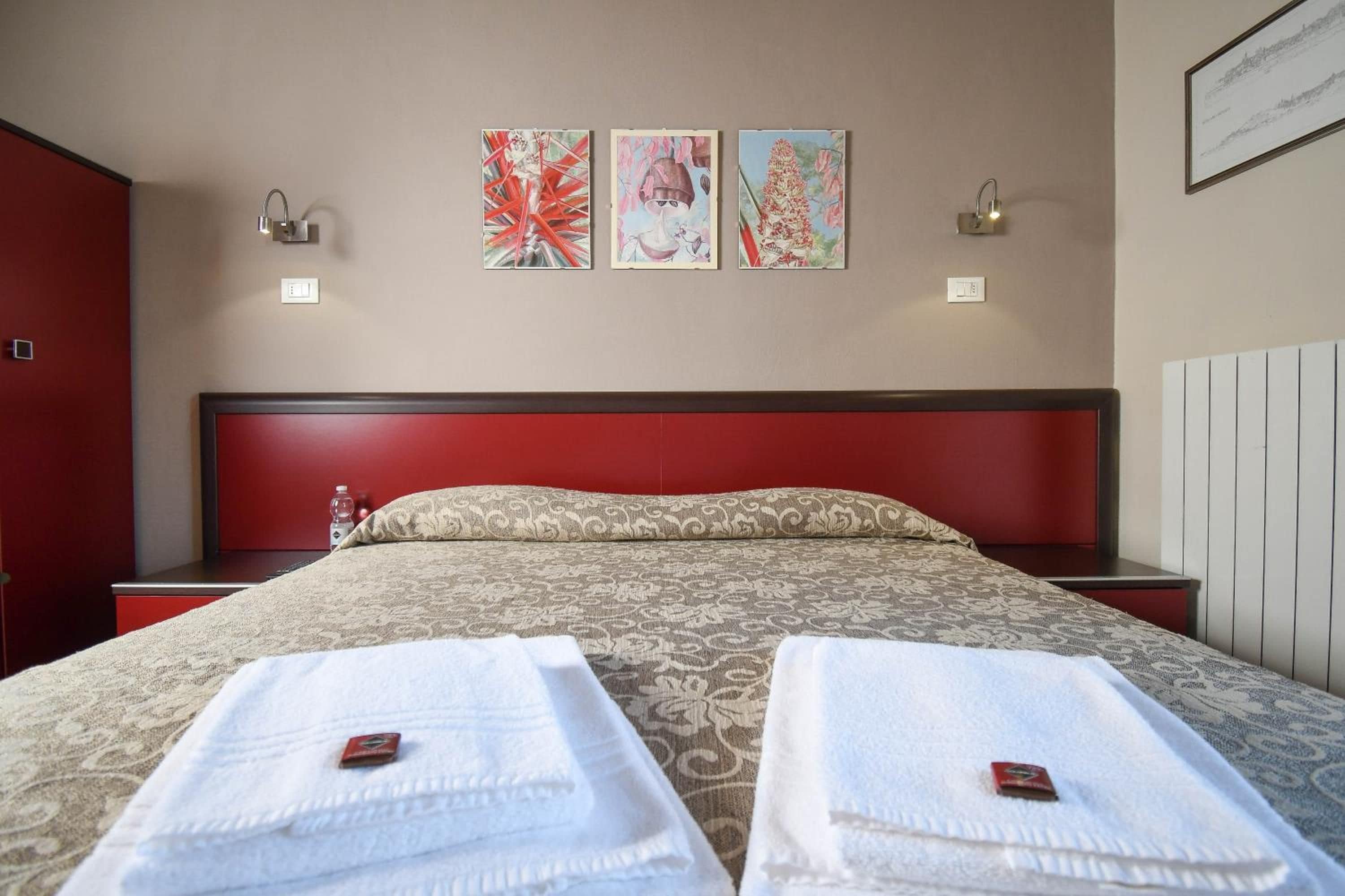 A hotel room with a large bed, two bedside tables, a red headboard, and three artworks on the wall.