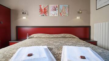 A hotel room with a large bed, two bedside tables, a red headboard, and three artworks on the wall.
