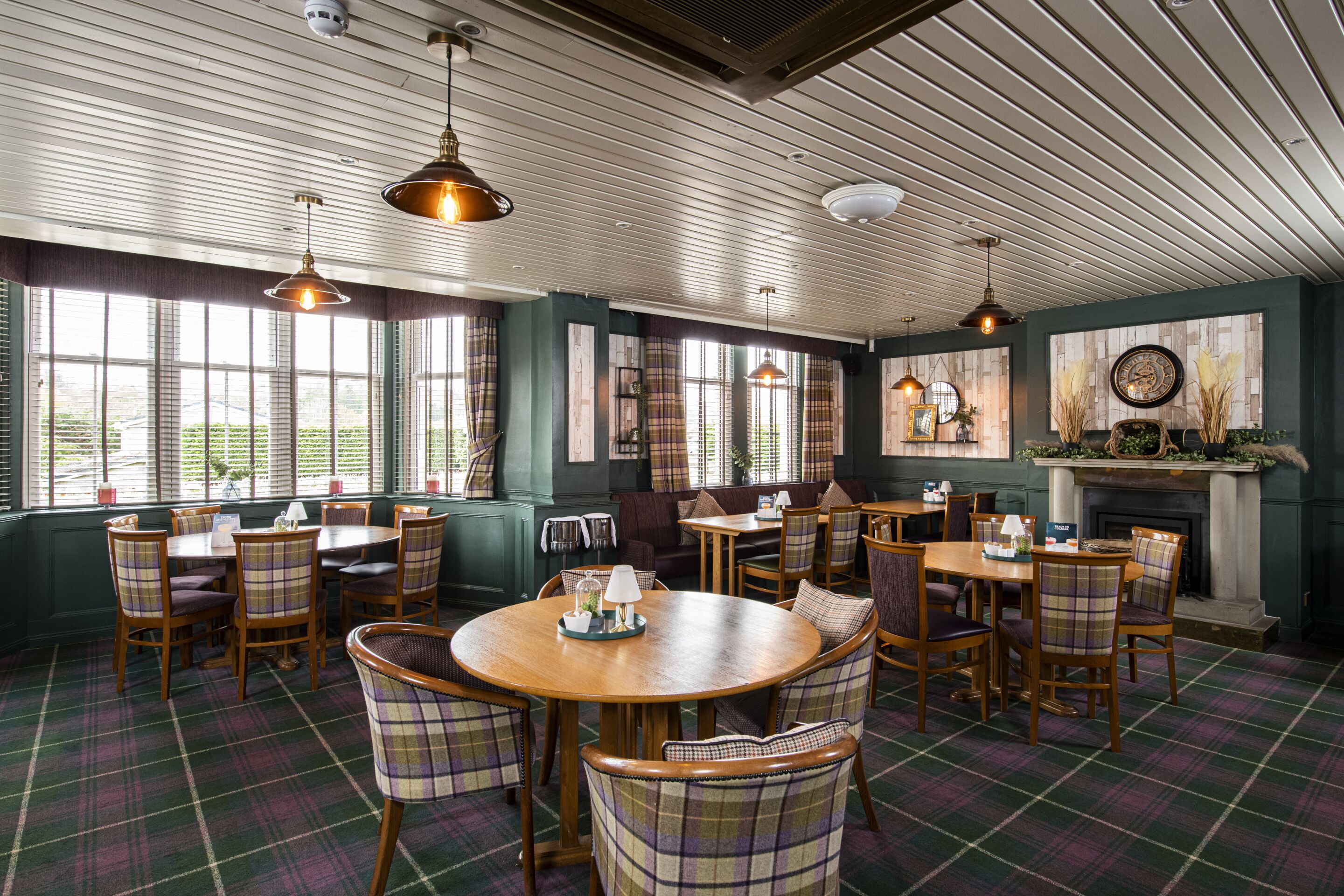A dining area with plaid-patterned chairs, wooden tables, and hanging pendant lights.