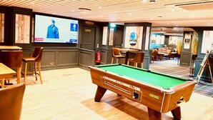 Una sala de billar con mesa de pool, sillas y una televisión que muestra un noticiero.