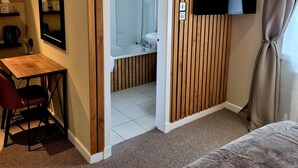 Habitación de hotel con pared decorativa de madera, ducha, escritorio con silla, televisor de pantalla plana y una ventana grande con cortinas.