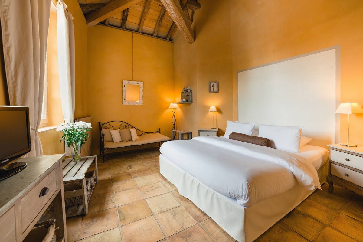 A bedroom with a large bed, bedside tables, a TV, and a window with curtains.