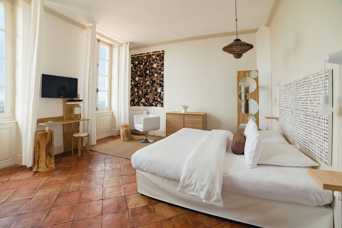 A bedroom with a large bed, a TV, a wooden desk, a chair, and a wall with circular mirrors.