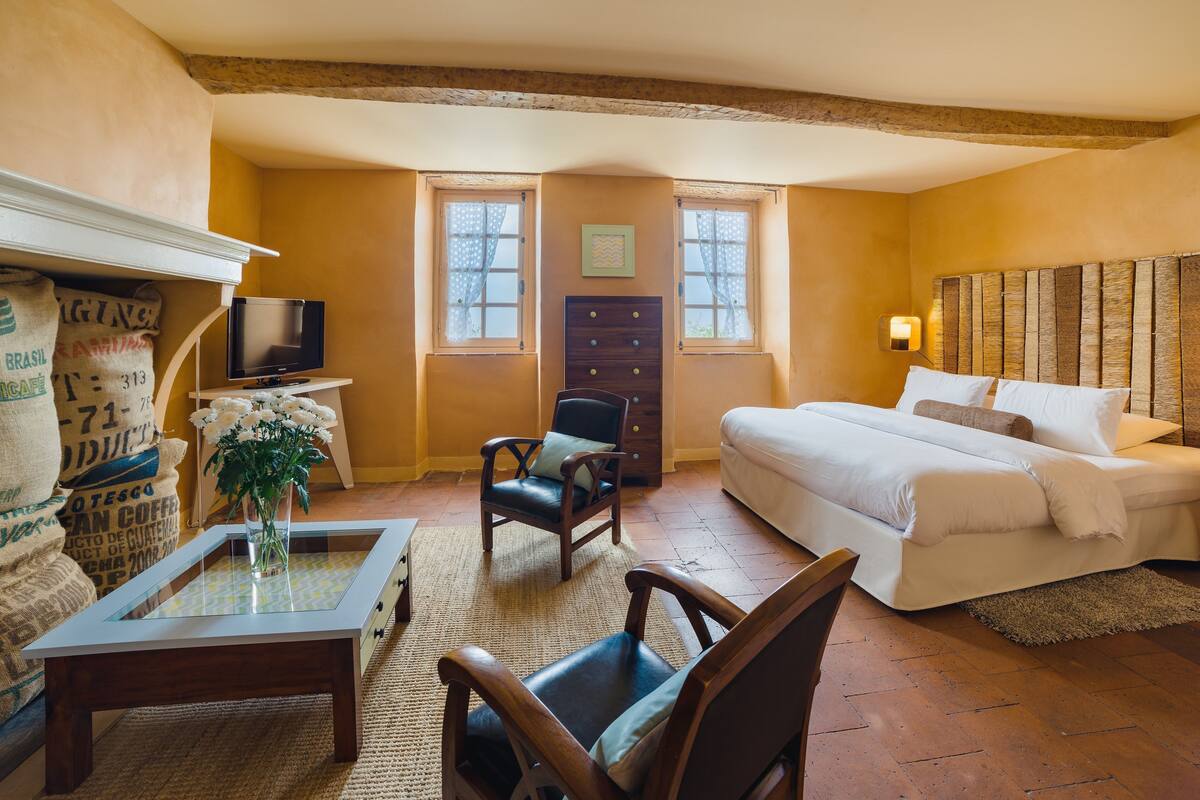 A cozy room with a bed, a TV, a wooden chair, a small table, and a window.