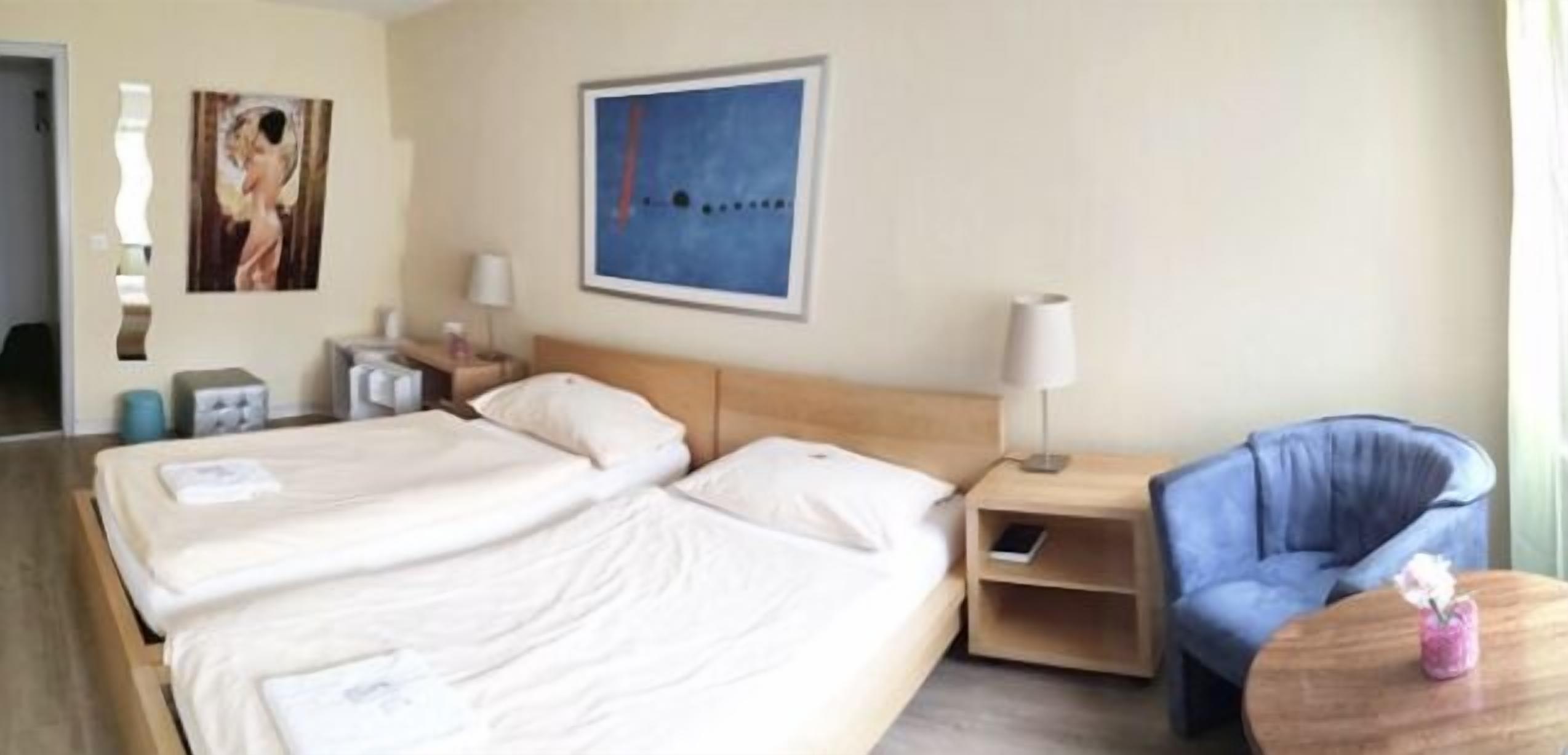 Ein Hotelzimmer mit zwei Betten, einem Nachttisch, einer Lampe, einem Sessel und einem Bild an der Wand.