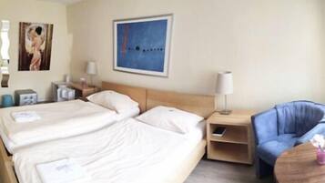 Ein Hotelzimmer mit zwei Betten, einem Nachttisch, einer Lampe, einem Sessel und einem Bild an der Wand.