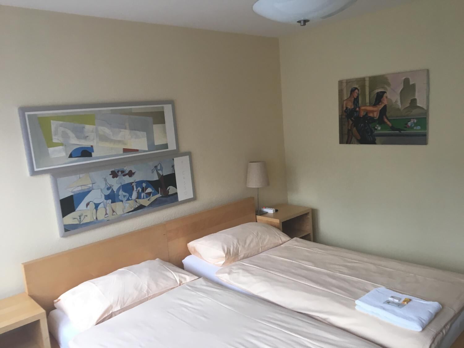 Habitación de hotel con cama, dos mesitas de noche, una lámpara y dos cuadros en la pared.