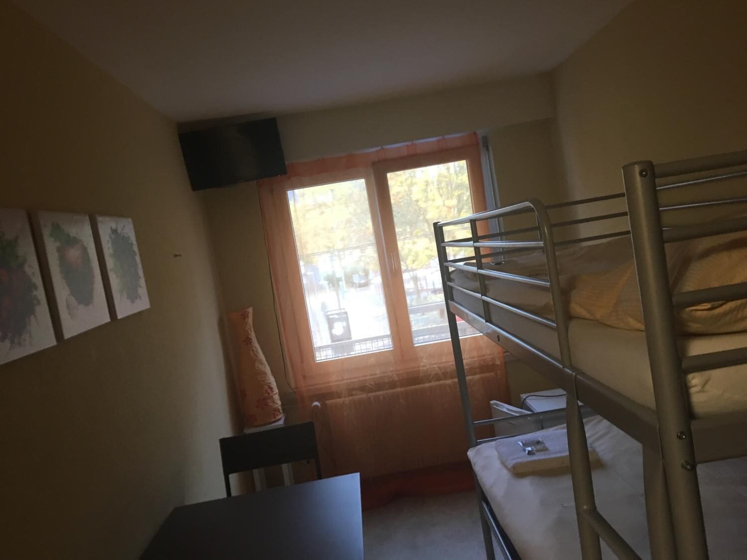 Quarto em dormitório com beliches, escrivaninha e janela com cortinas.