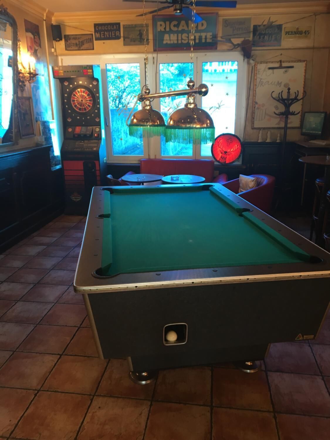 Una mesa de billar en una sala con un dardo, un reloj y un letrero que dice "Ricard Anisette".