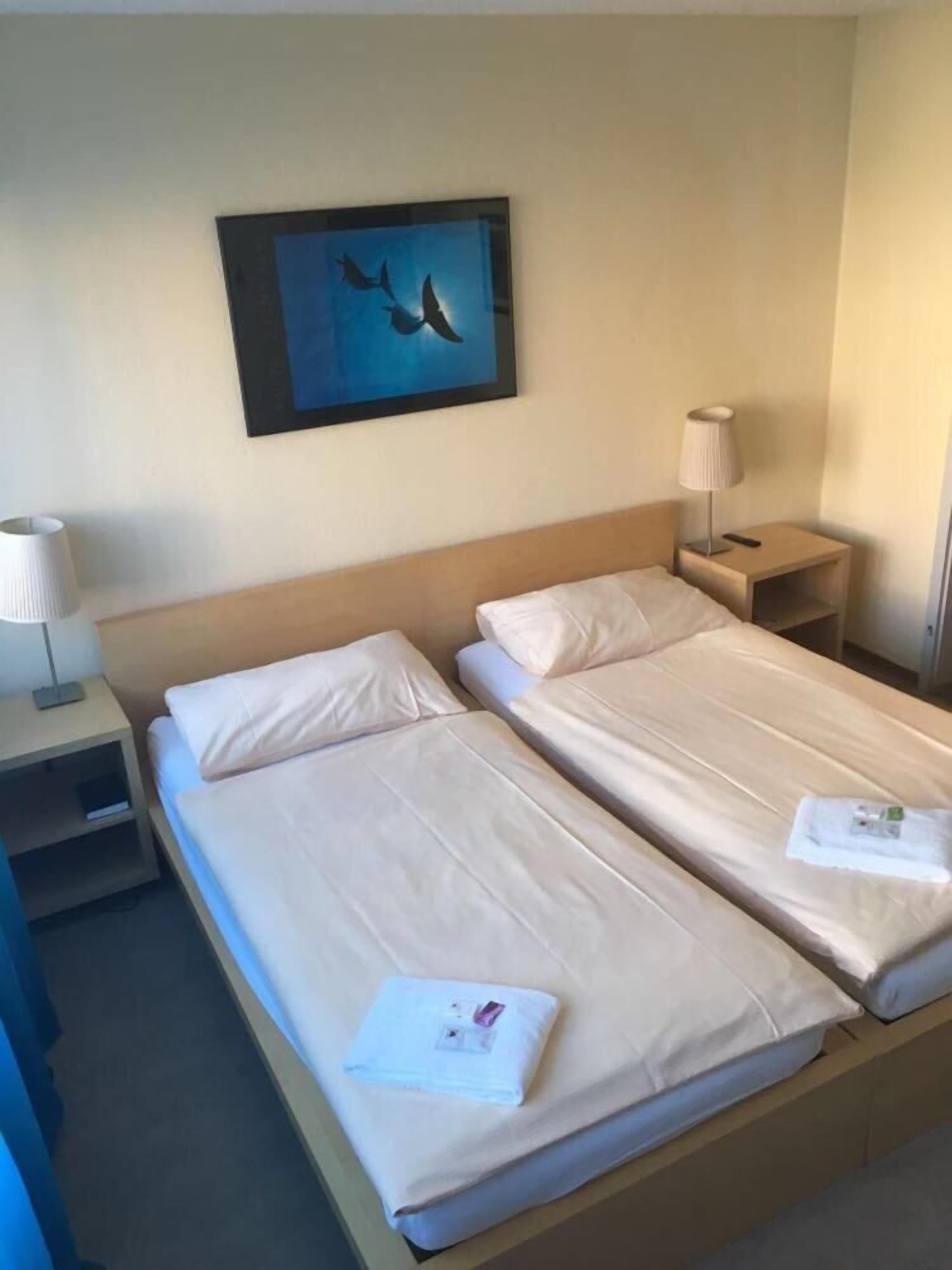 Ein Hotelzimmer mit einem Doppelbett, einem Nachttisch mit Lampe und einem gerahmten Bild an der Wand.