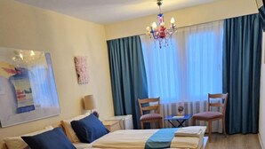 A double bed with a blue bedspread, a wooden nightstand, a chair, a small table, and a chandelier. - Hotel & Backpackers Zak (Neuhausen am Rheinfall)