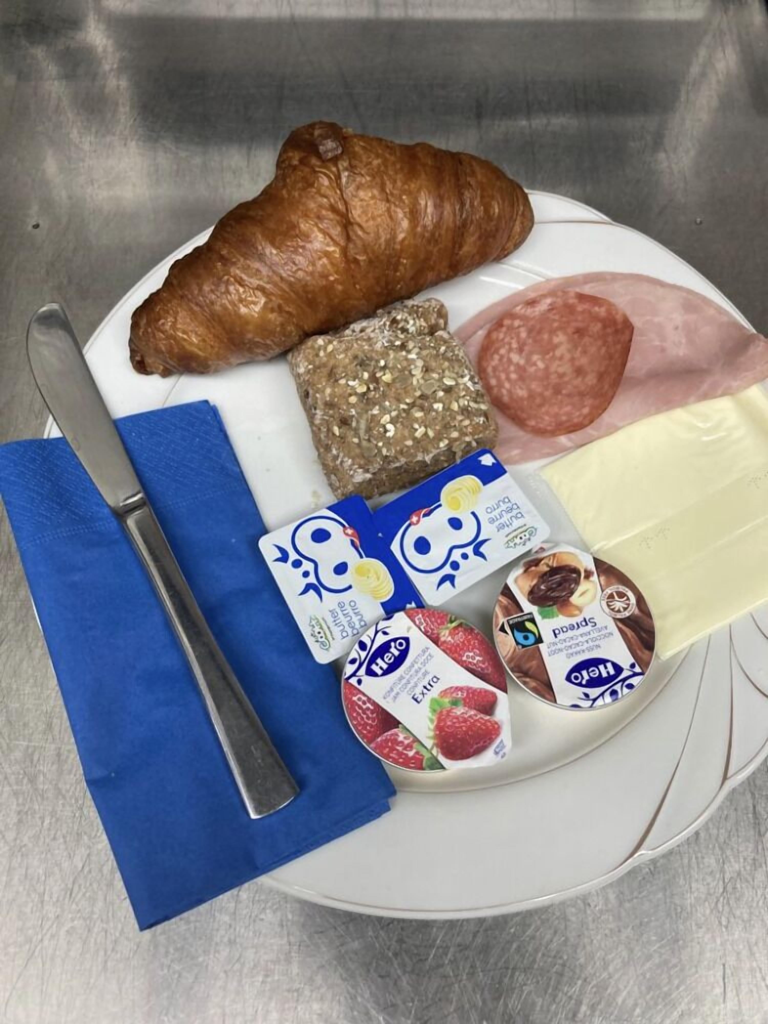 A plate with a croissant, a slice of ham, a piece of cheese, and two yogurt containers.