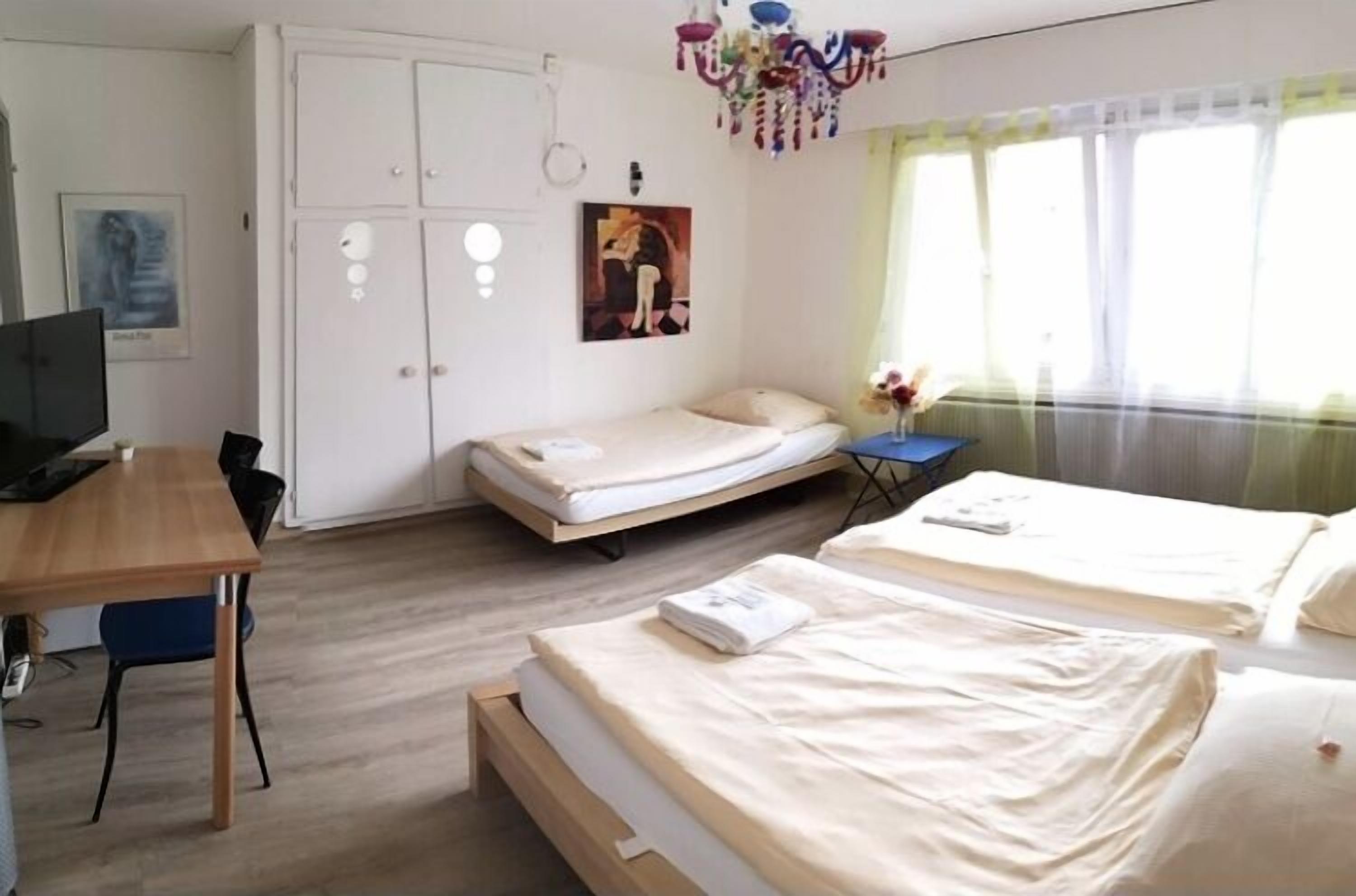A hotel room with a desk, two beds, a wardrobe, and a window with curtains.