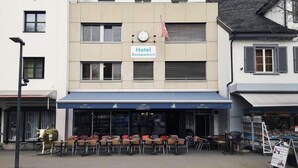 A hotel with a sign reading "Hotel Backpackers" and outdoor seating with tables and chairs. - Hotel & Backpackers Zak (Neuhausen am Rheinfall)