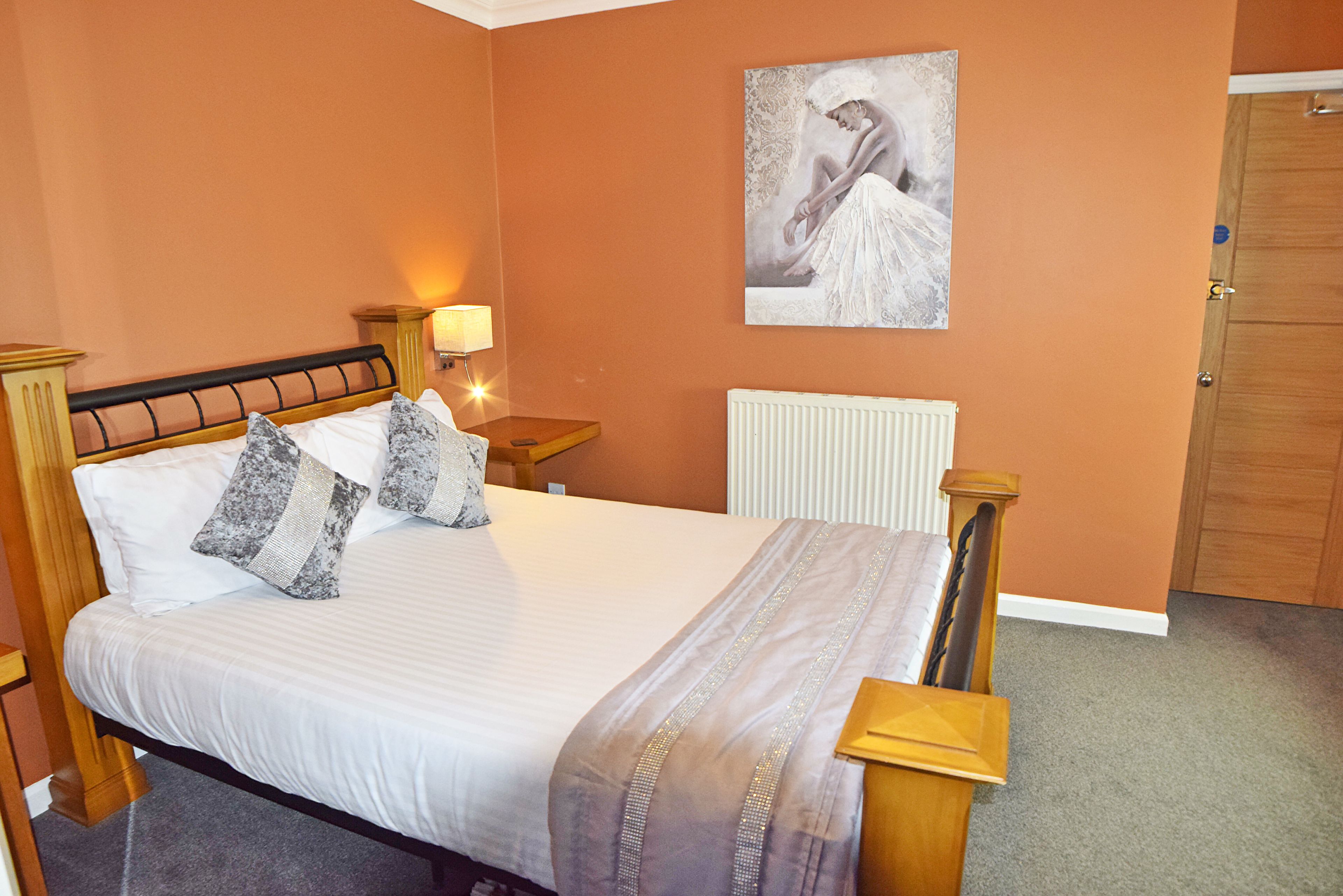 A neatly made bed with a headboard, a bedside table with a lamp, and a radiator.