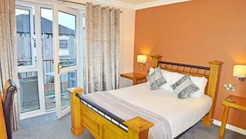 A bedroom with a bed, two bedside tables, a window with curtains, and a view of the outside.