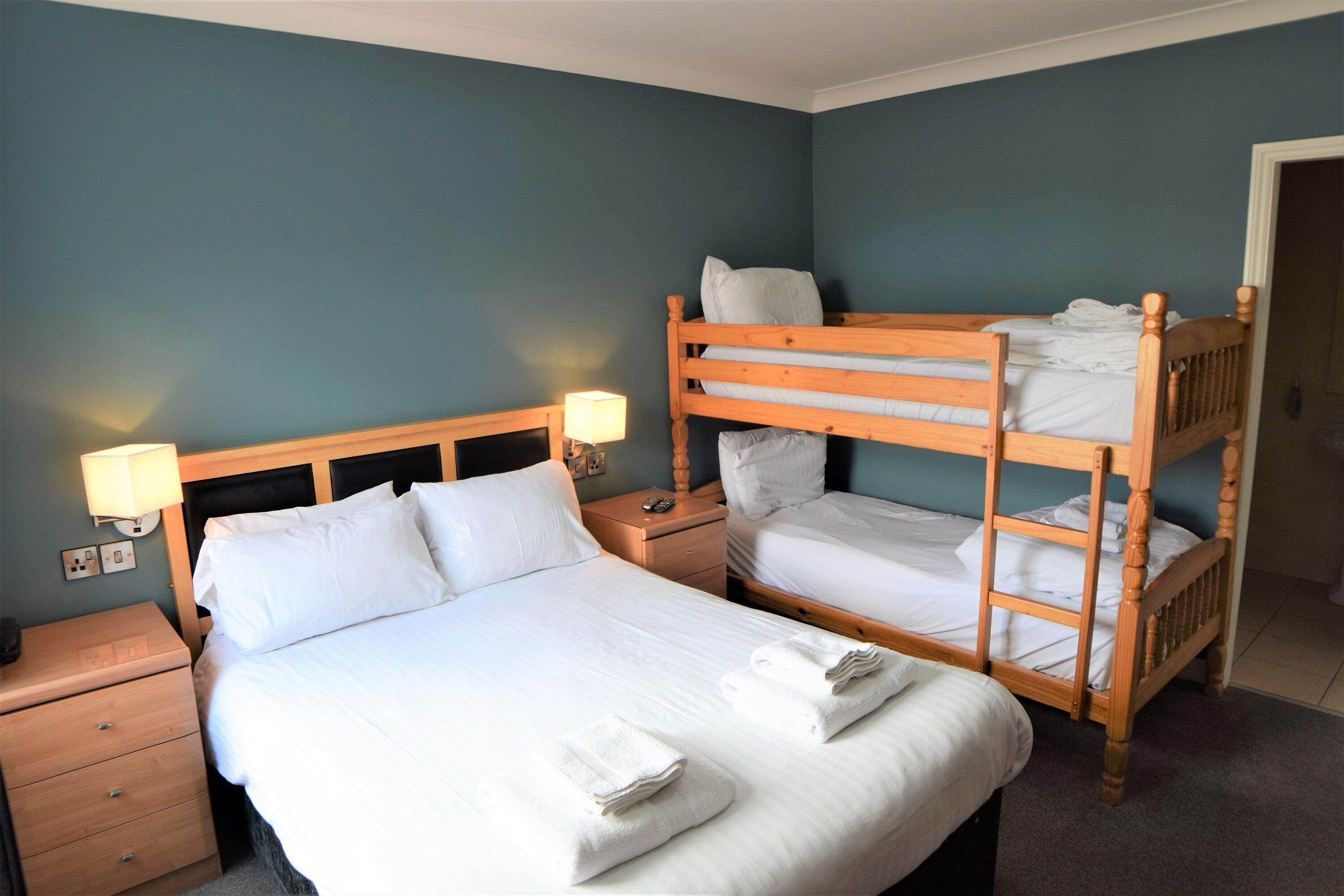 Una habitación de hotel con una cama individual, una cama nido de madera, una mesita de noche con lámpara y una unidad de cajones.