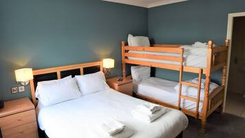 Una habitación de hotel con una cama individual, una cama nido de madera, una mesita de noche con lámpara y una unidad de cajones.