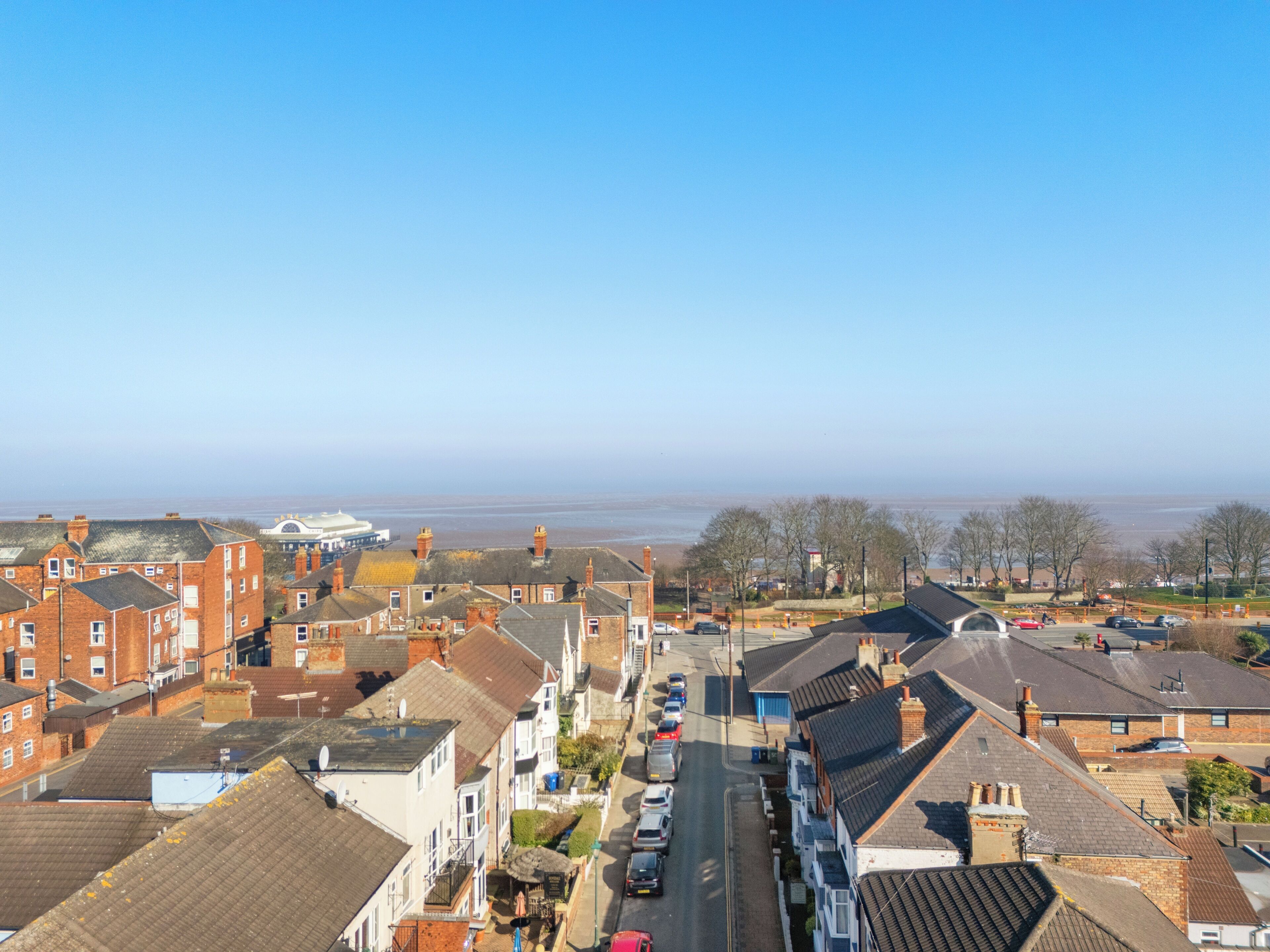 A residential street with houses, a clear sky, and a distant view of the sea.