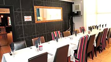 Un comedor con una larga mesa dispuesta para una comida, sillas con cojines a rayas, un espejo en la pared y un cartel que anuncia un menú a mitad de precio.