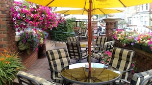 Een buitenruimte met geruite stoelen en een gele parasol, omgeven door bloempotten.