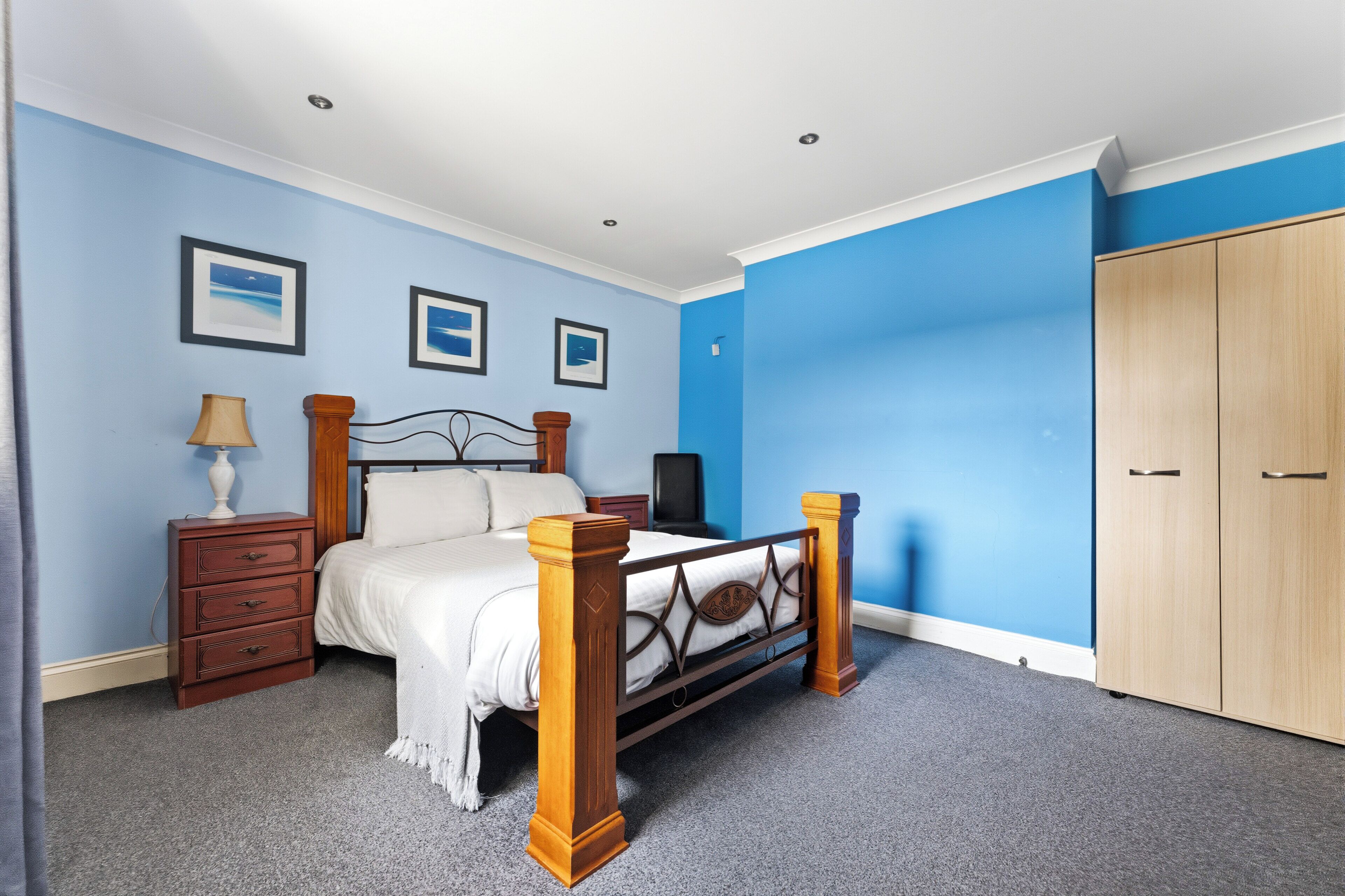 Une chambre à coucher comprenant un lit, une commode, une armoire et des tableaux encadrés accrochés au mur.