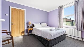 A bedroom with a bed, a nightstand, a lamp, a chair, a window with curtains, and a door.