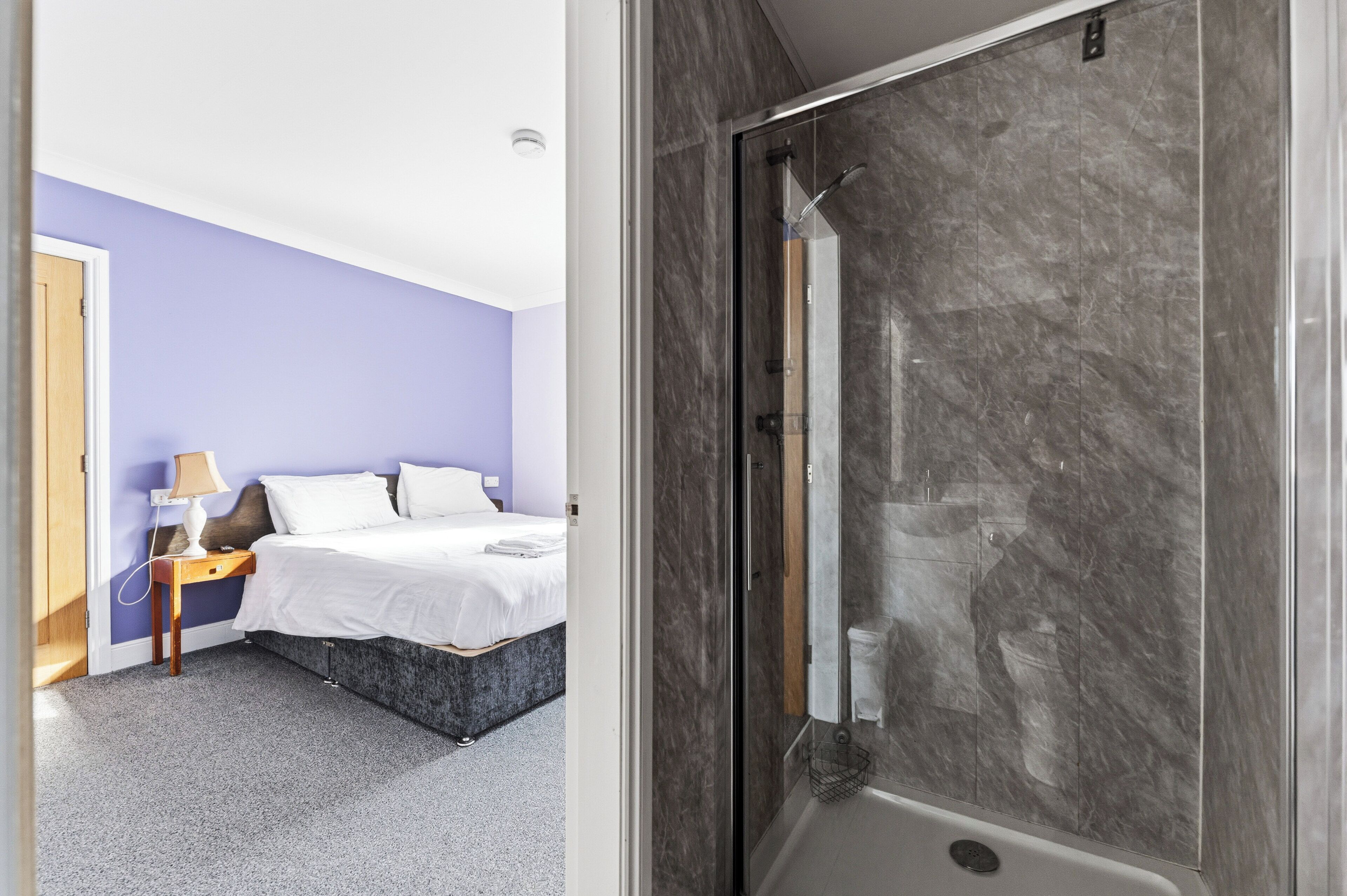 A room with a bed, a nightstand, a lamp, and a shower area with a glass door.