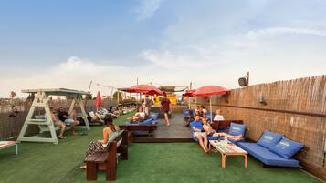 An outdoor patio area with seating arrangements, including benches and lounge chairs, under red umbrellas.