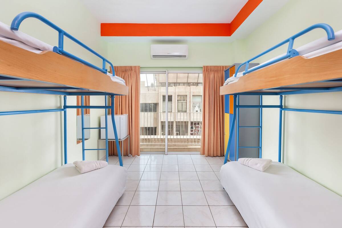 A dormitory room with bunk beds, a window with curtains, and an air conditioning unit.