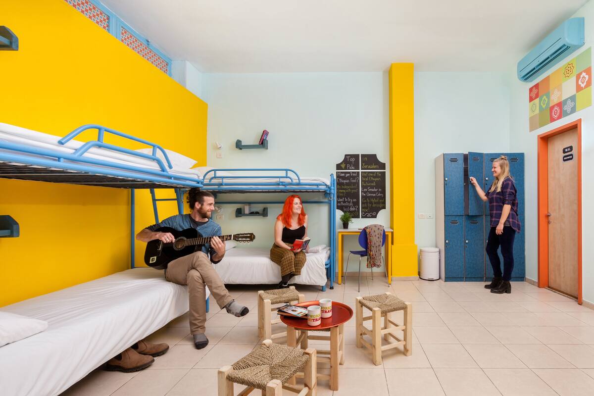A dormitory room with bunk beds, a small table with mugs, and a chair.