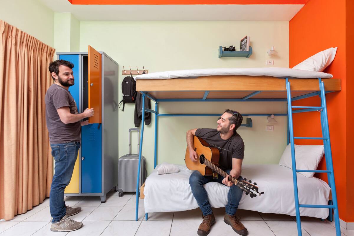 A dormitory room with bunk beds, a suitcase, and a guitar.
