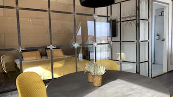 A modern room with a round table, yellow chairs, a bed with a wooden headboard, and a large window.