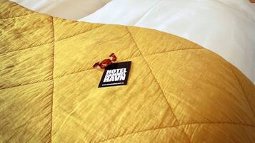 A hotel room with a bed featuring a yellow quilted bedspread, white pillows, and a black tag on the bed.