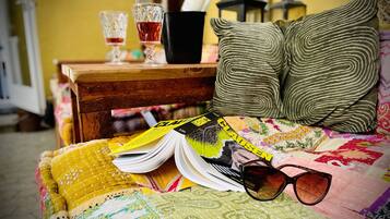 A bed with a quilt, a magazine, a pair of sunglasses, and a bottle of perfume on a wooden nightstand.