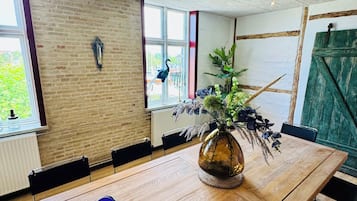 Une salle de conférence avec une longue table en bois, des chaises, un vase avec des plantes et une fenêtre donnant sur un paysage verdoyant.