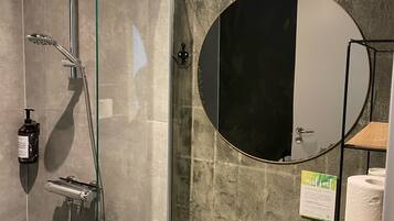 A modern bathroom with a glass-enclosed shower, a white sink, a round mirror, and a wall-mounted light fixture.