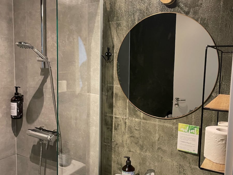 A modern bathroom with a glass-enclosed shower, a white sink, a round mirror, and a wall-mounted light fixture.
