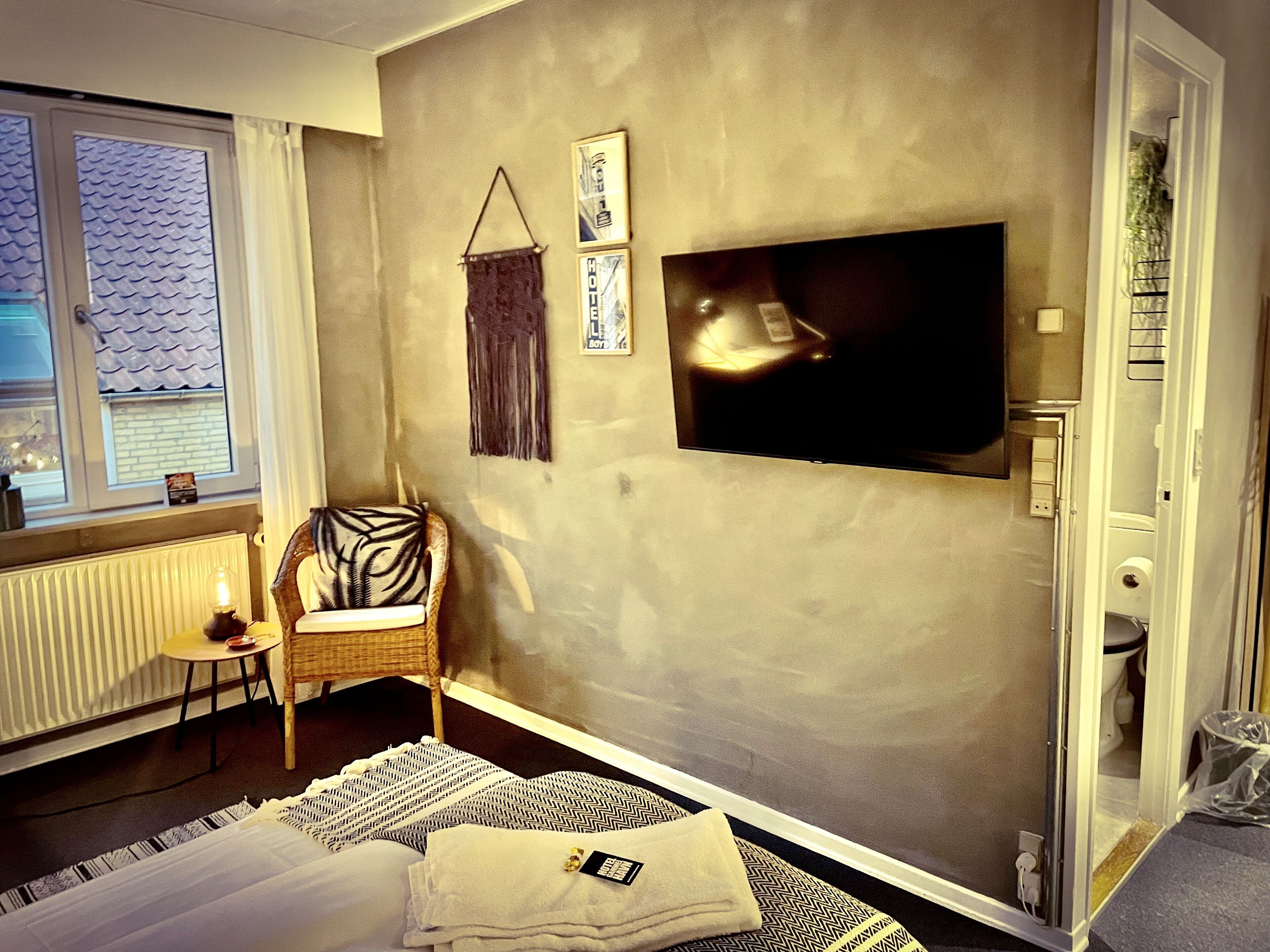 Ein Hotelzimmer mit Bett, Sessel, Wandfernseher und Fenster mit Blick ins Freie.