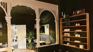 A room with a wooden table, chairs, a bookshelf, and a mirror. There is a potted plant and framed pictures on the wall.