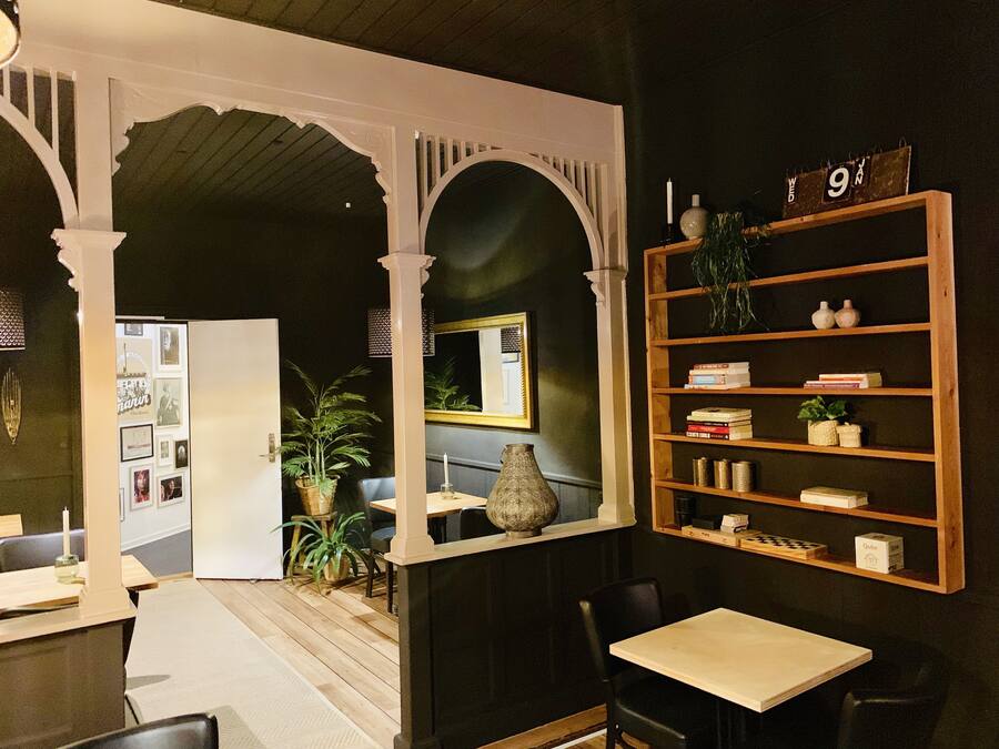 A room with a wooden table, chairs, a bookshelf, and a mirror. There is a potted plant and framed pictures on the wall.