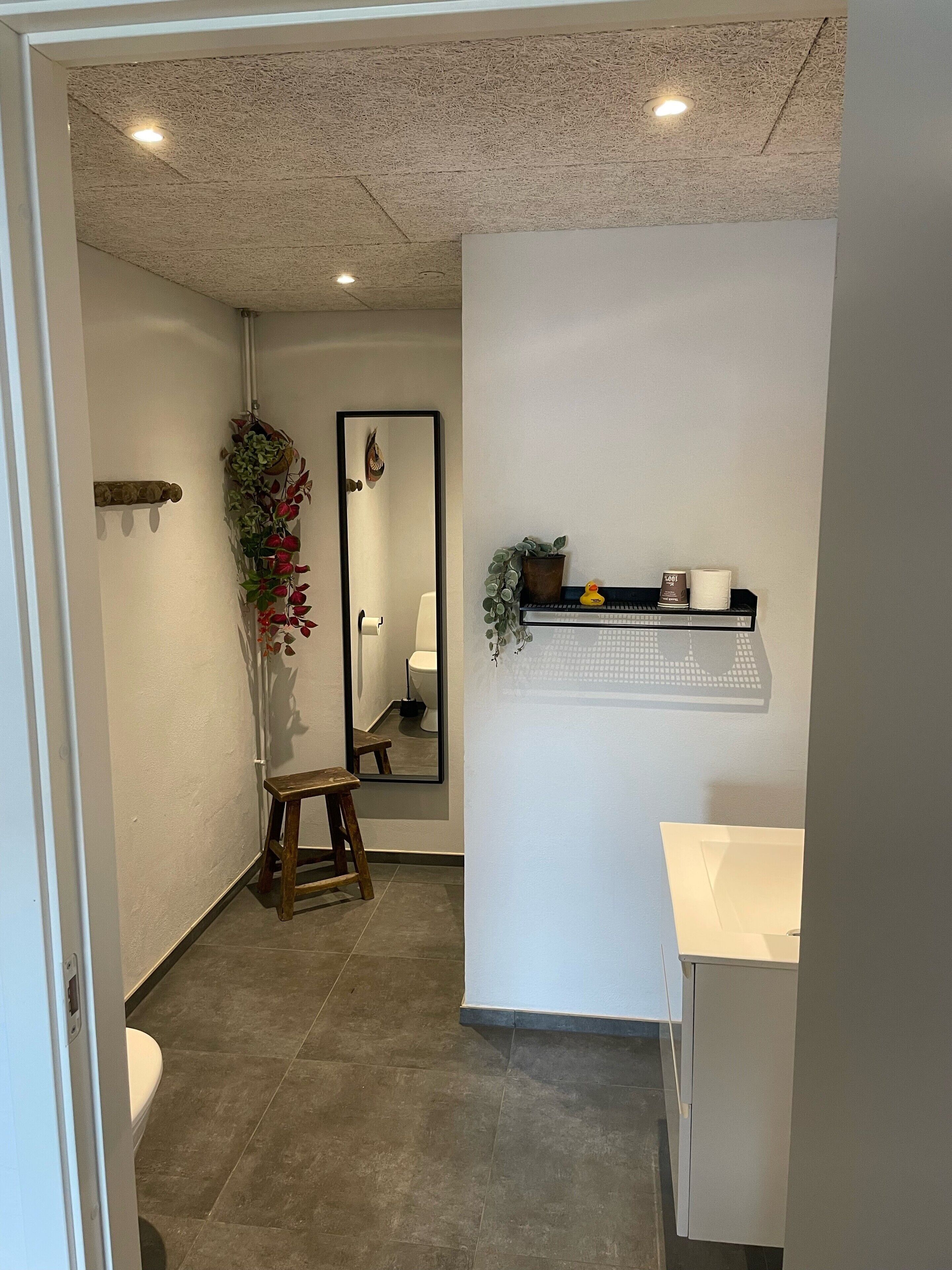 Un baño con inodoro, lavamanos, espejo y estante con artículos de aseo.