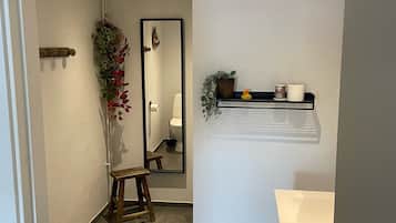 Un baño con inodoro, lavamanos, espejo y estante con artículos de aseo.