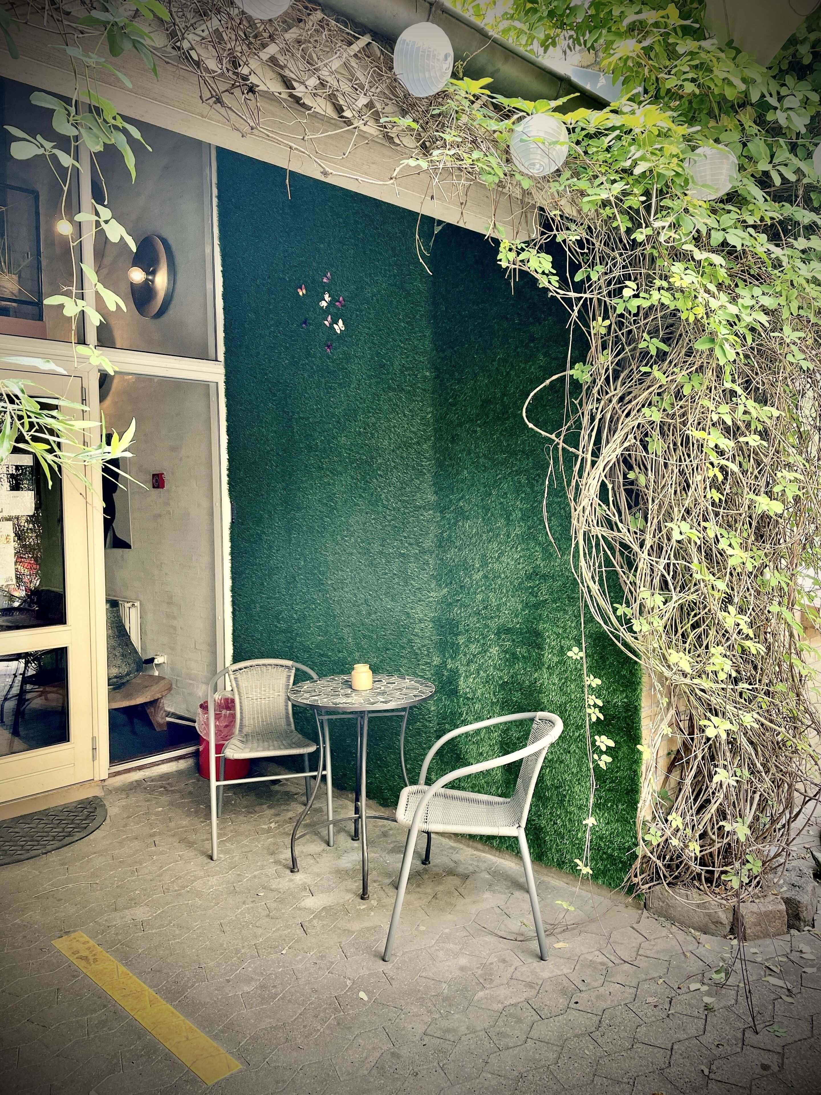 An outdoor seating area with two chairs and a table, a green wall, and a potted plant.